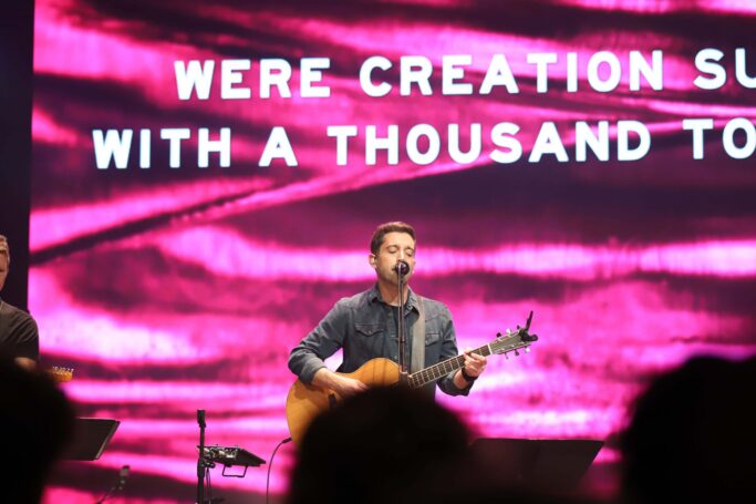 Demi Tebow and another man perform a special vocal duet on stage at the chapel, singing the powerful words "we're creation survivor" with their thousand tongues.