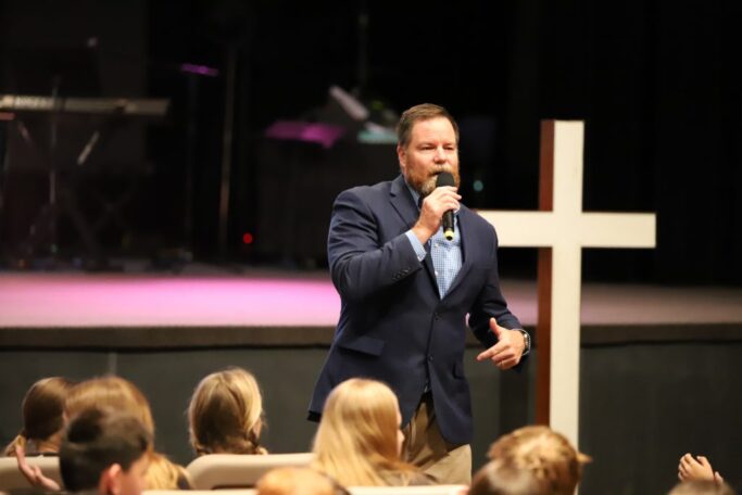 A man speaking into a microphone in front of an audience, engaging in civic discourse.