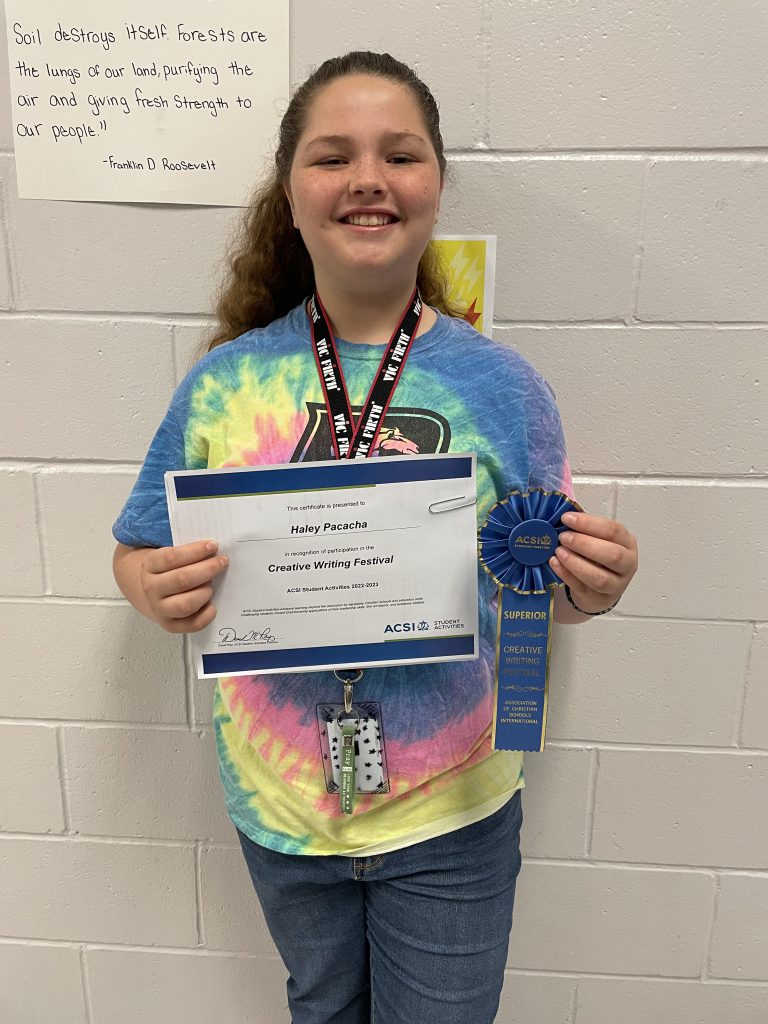A girl proudly displaying her Creative Writing Contest Award certificate in front of a wall, representing her accomplishment in the prestigious ACSI competition.
