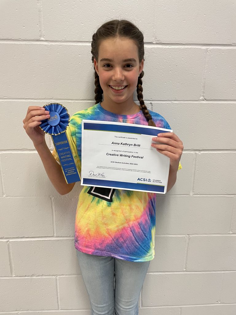 A girl proudly displaying an awards ribbon in front of a wall.