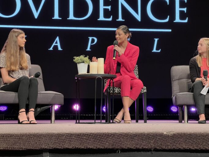 Three women sitting in chairs on stage with the words Alabama.