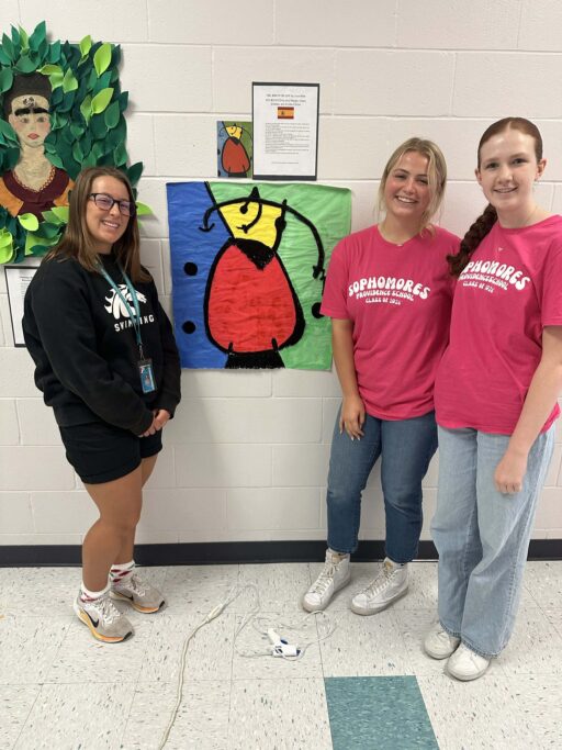 Three students in pink shirts standing in front of a wall, showcasing elements of Hispanic culture.