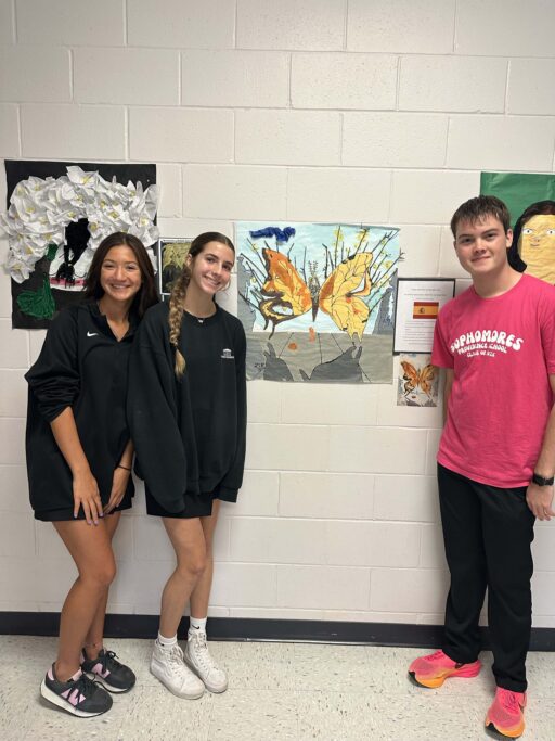 Three Hispanic students standing in front of a wall with artwork.