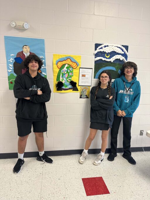 Three Spanish students standing in front of a wall with art on it, showcasing Hispanic culture.