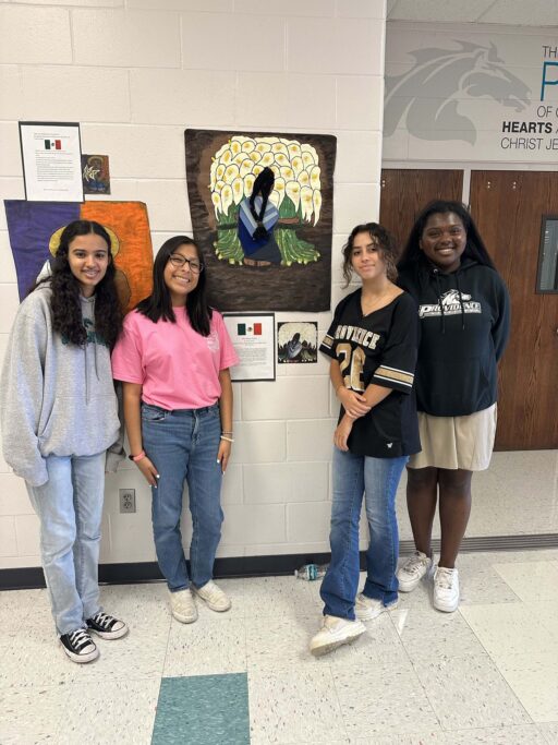 Four Spanish students celebrate in front of a wall with artwork.