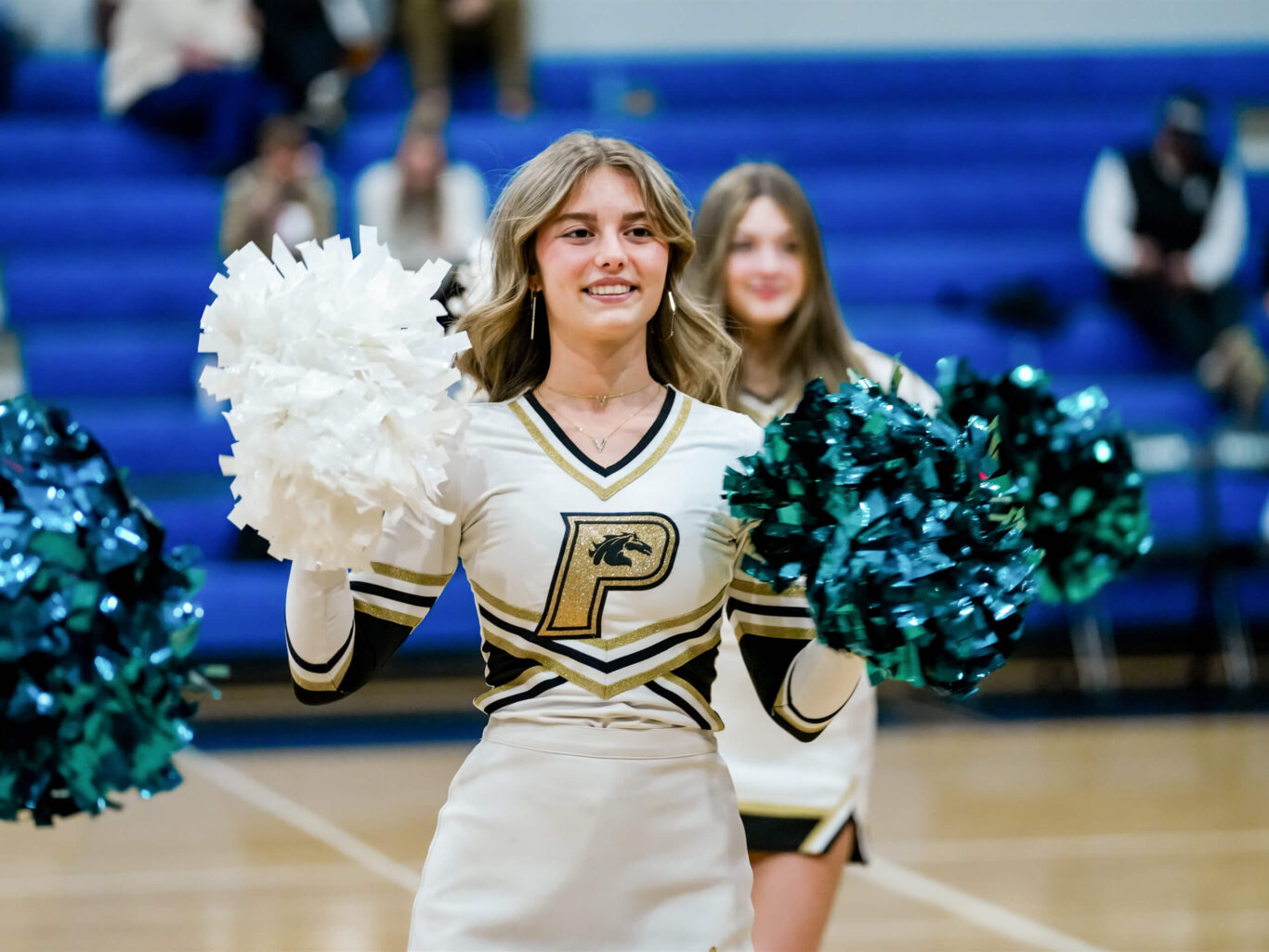 Two competitive cheerleaders on a basketball court with pom poms.