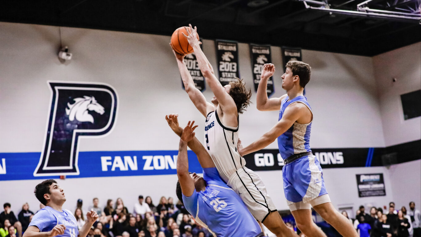 A group of boys playing basketball and trying to block the ball.