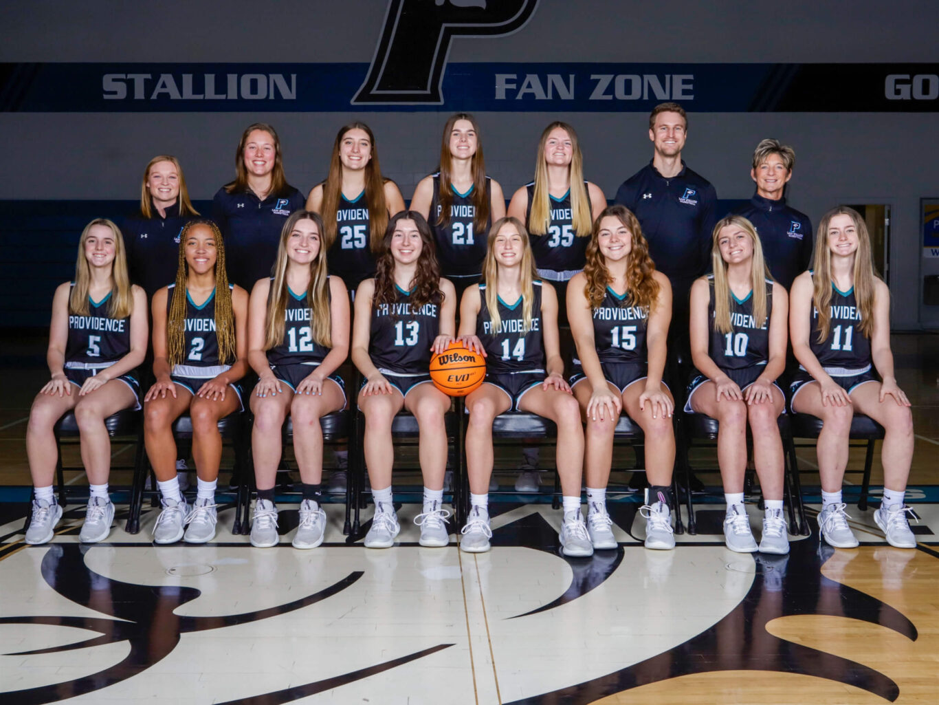 The girls basketball team is posing for a picture on the basketball court.