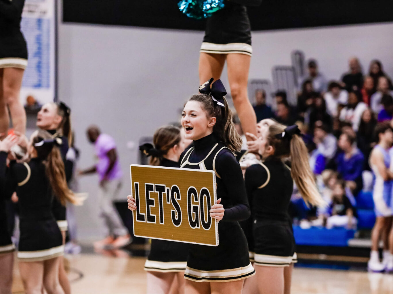 A competitive cheerleader holds up a sign that says let's go.