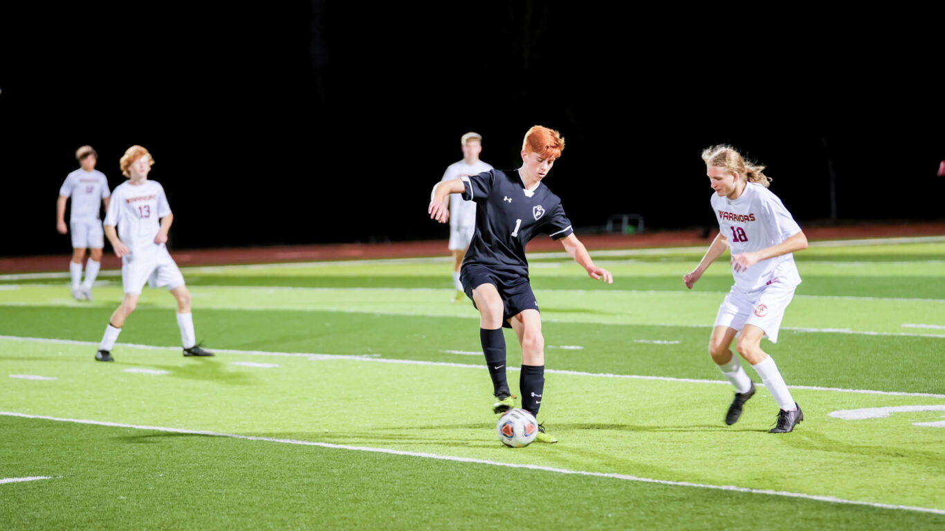 Two soccer boys kicking the ball on a field at night.