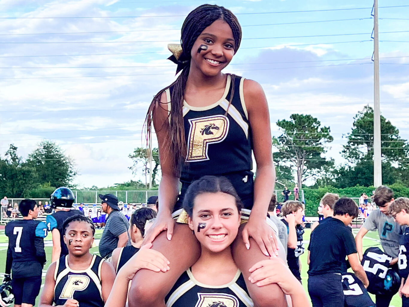 Two competitive cheerleaders sitting on top of each other at a football game.