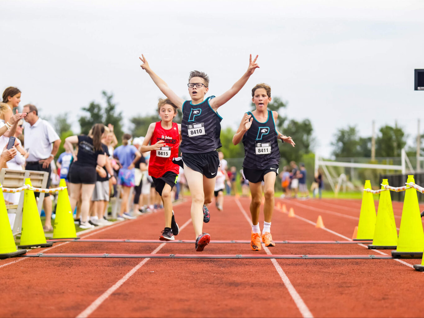 A group of boys participating in cross country, running on a track with cones in the background.