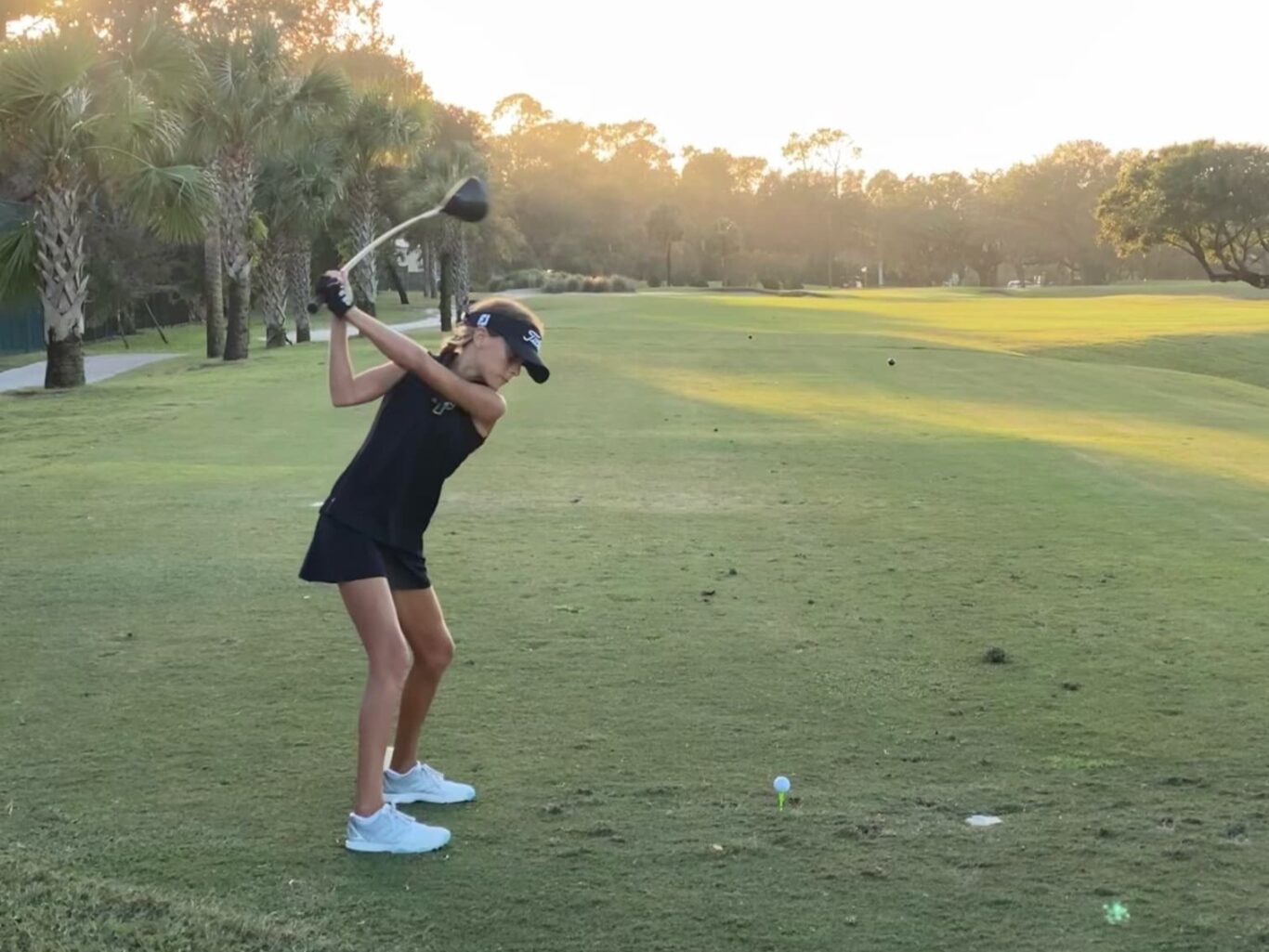 A girl swinging a golf club at sunset.