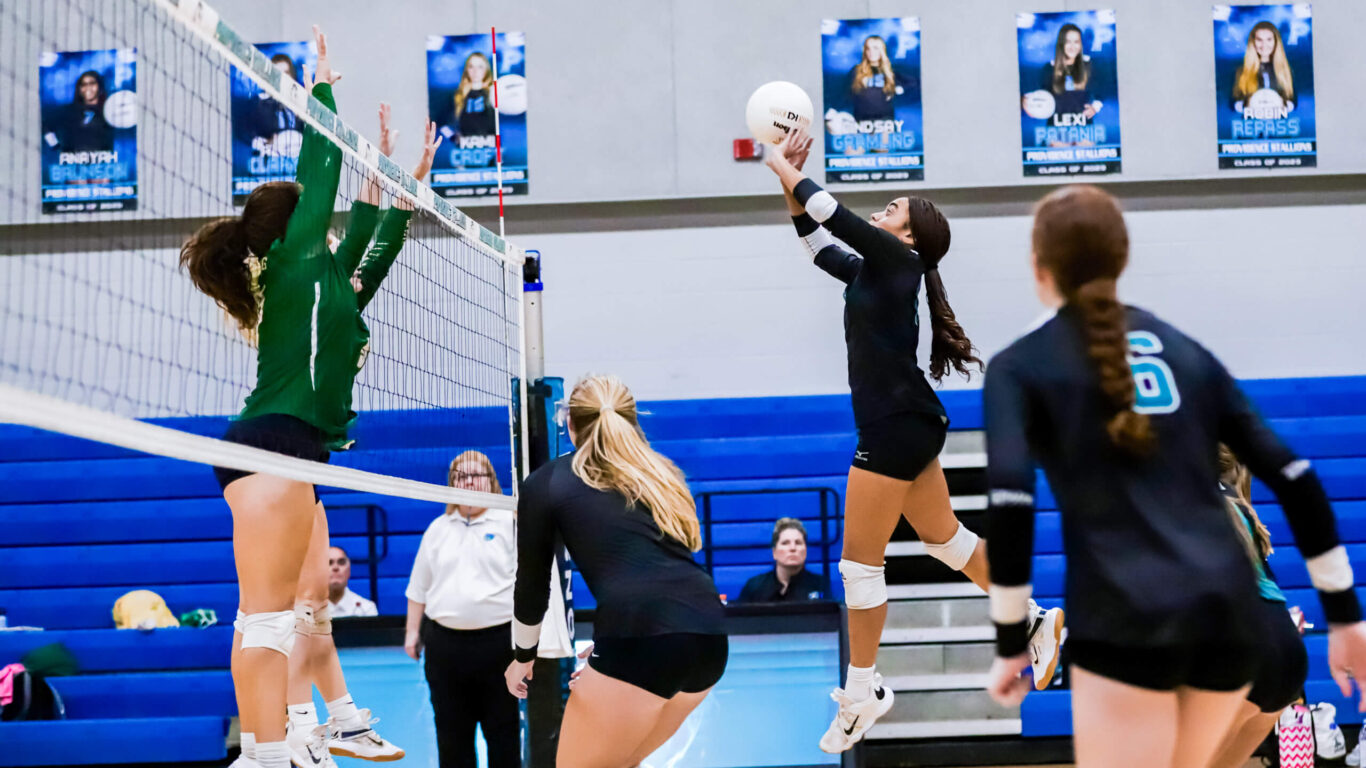 A girls' volleyball player jumps up to hit the ball.