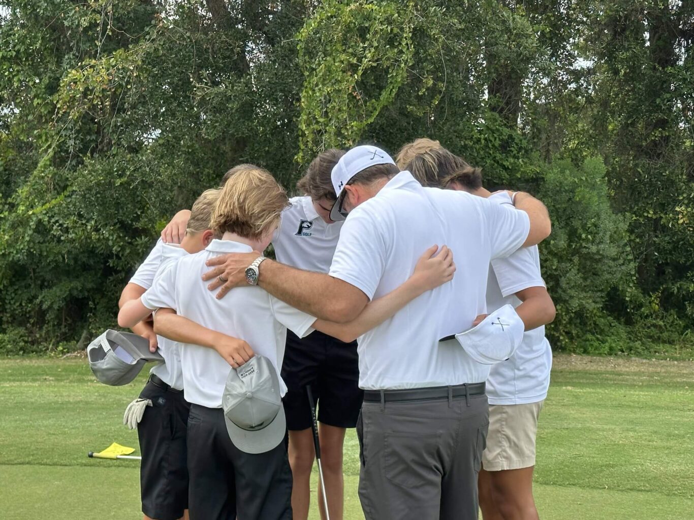 A group of boys huddle together on a golf course.