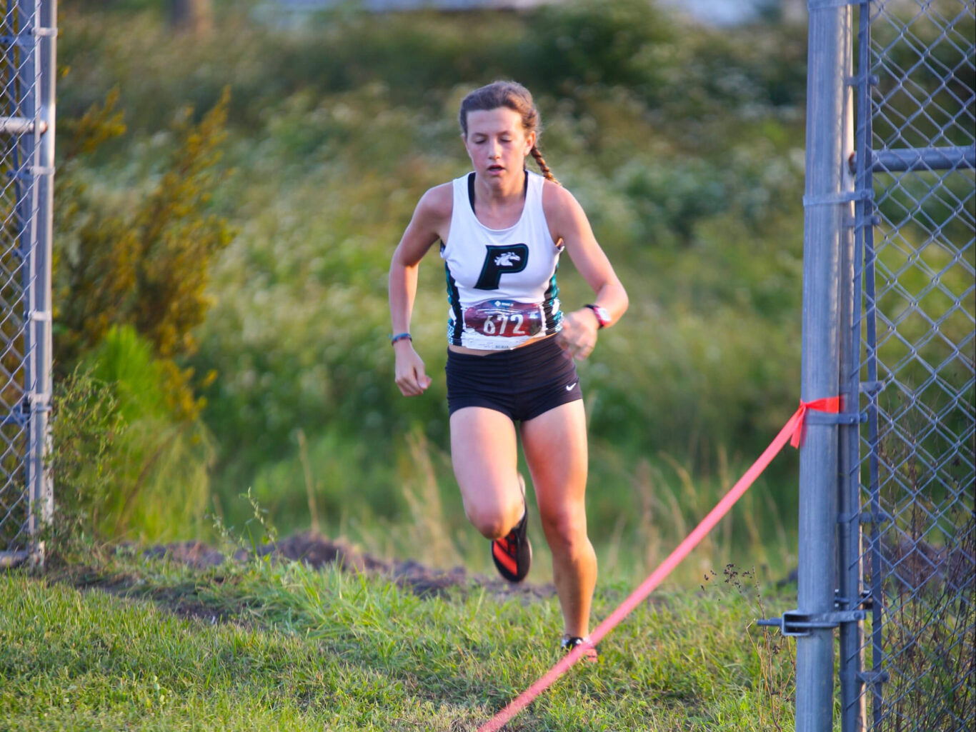 A cross country race participant, a girl, is running enthusiastically.