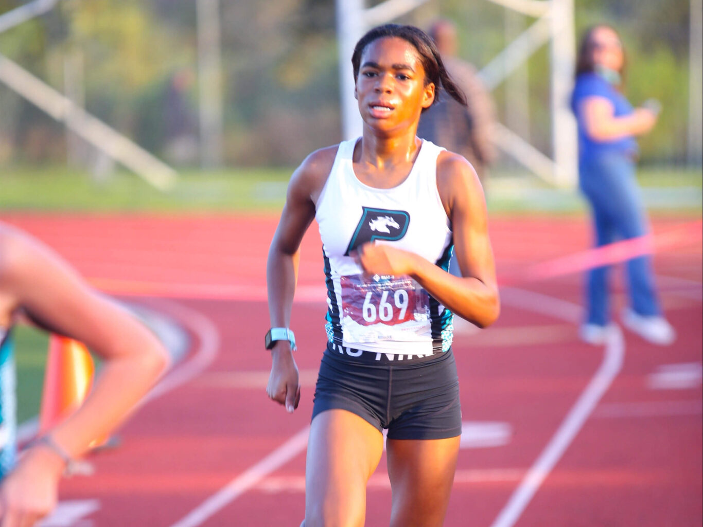 A girl sprinting on a track during a cross country race.