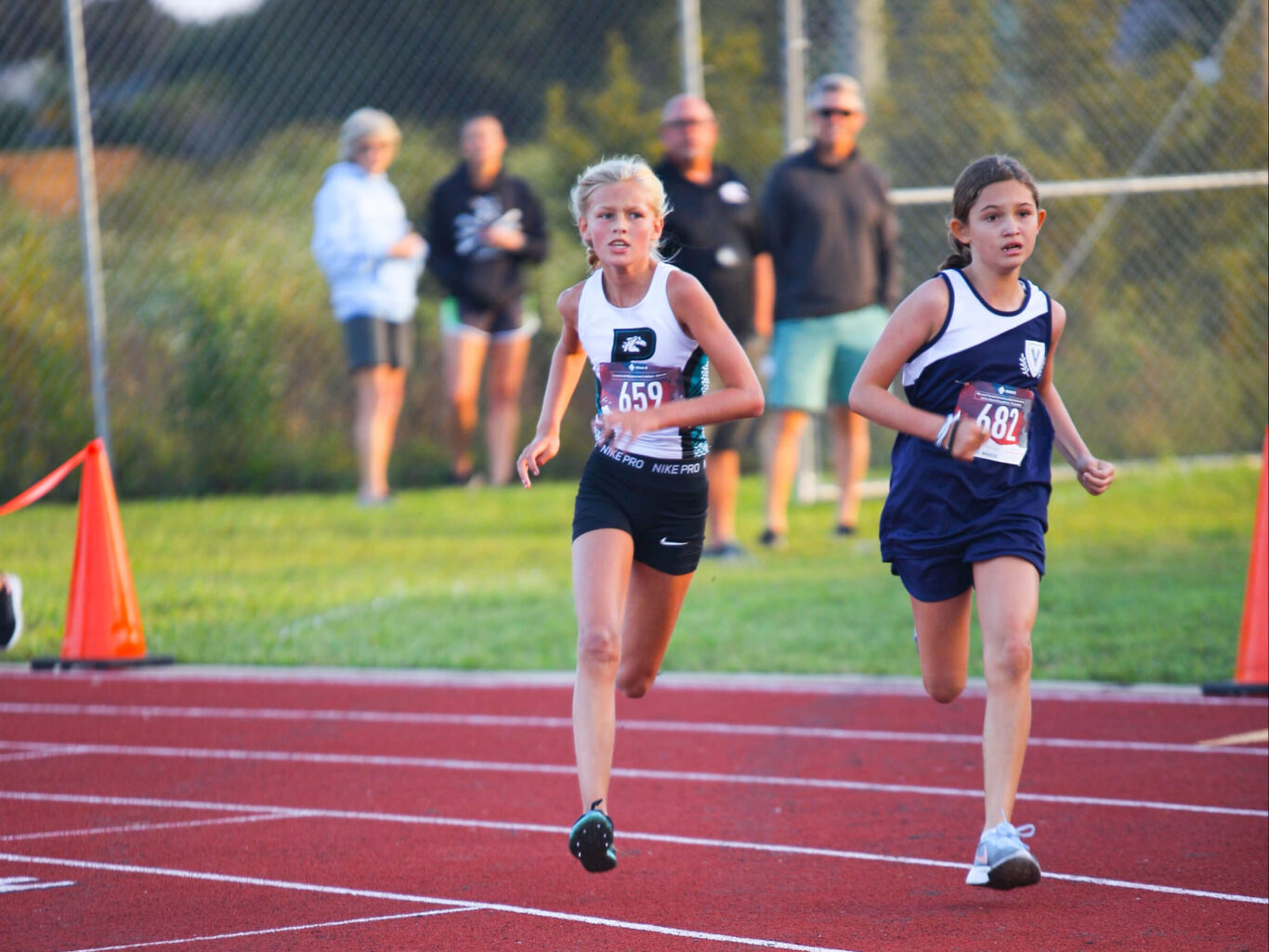 Two girls participating in a cross country race on a track.