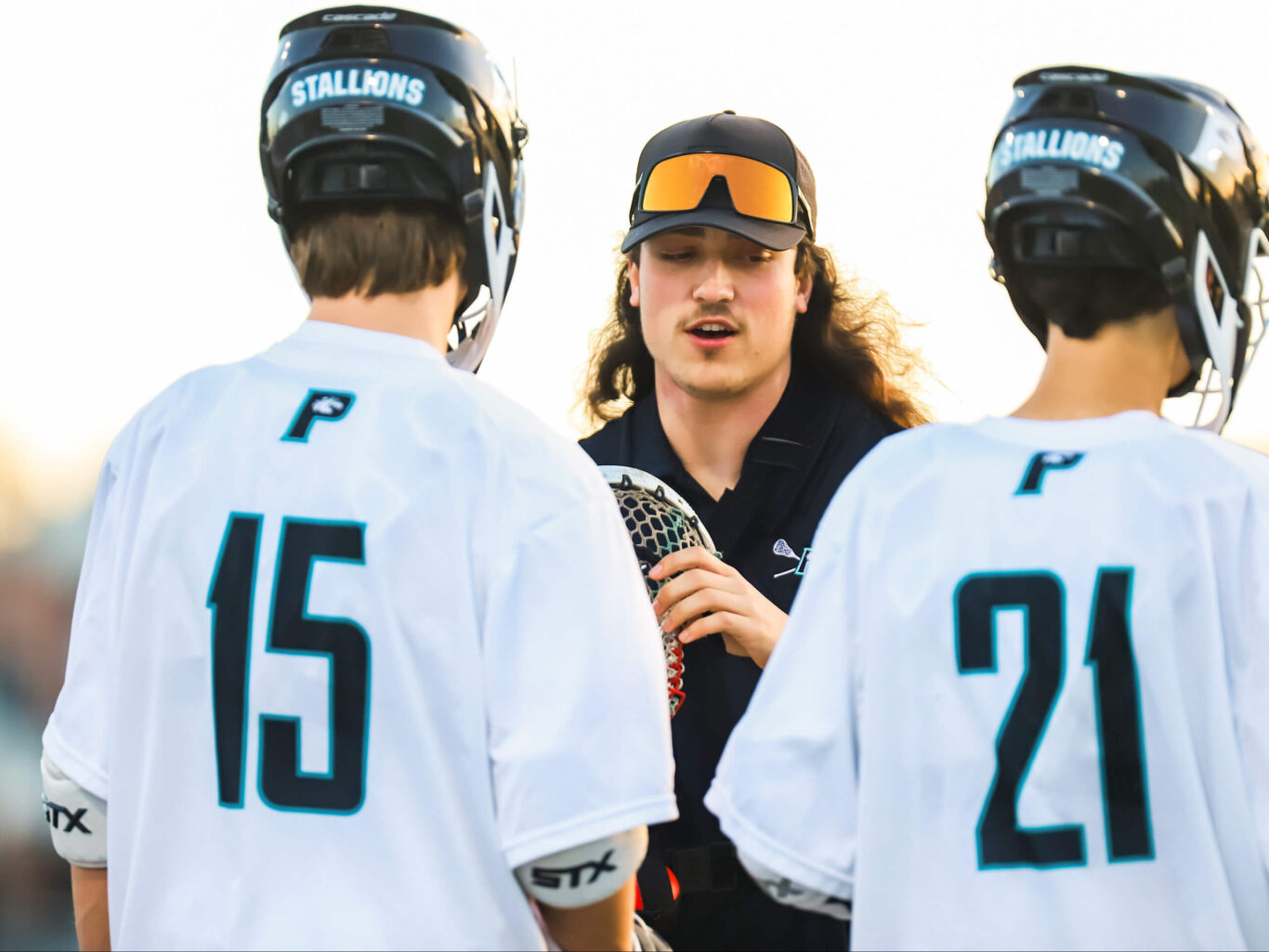 A group of lacrosse players, predominantly boys, conversing with each other.