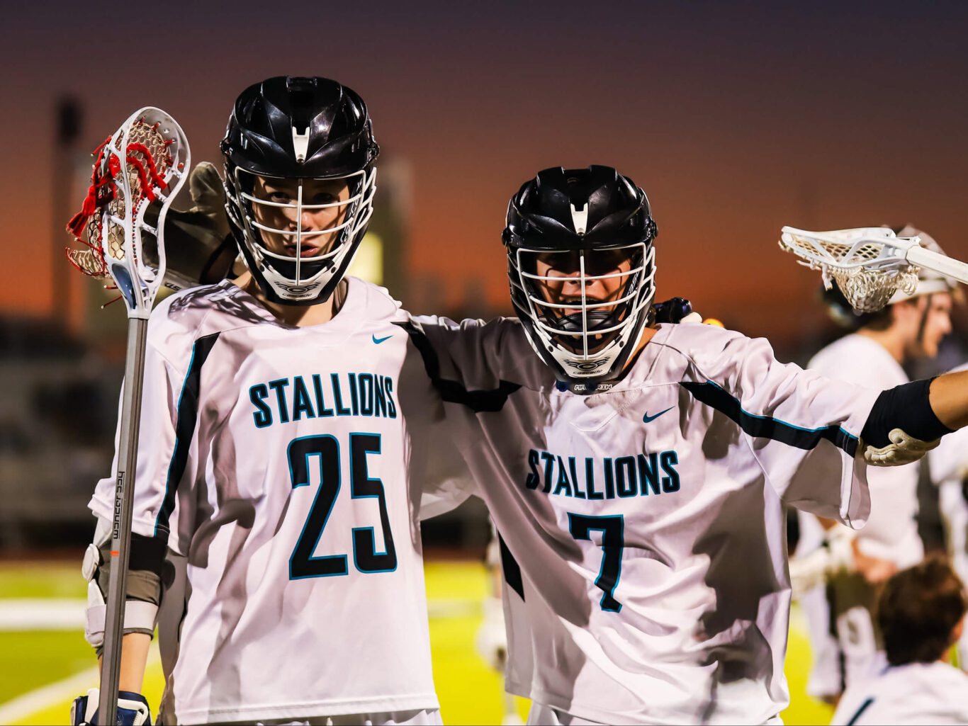 Two boys are holding up their lacrosse sticks.
