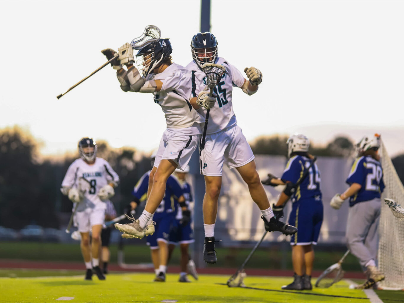 Two lacrosse players celebrating a goal during a game played by boys.