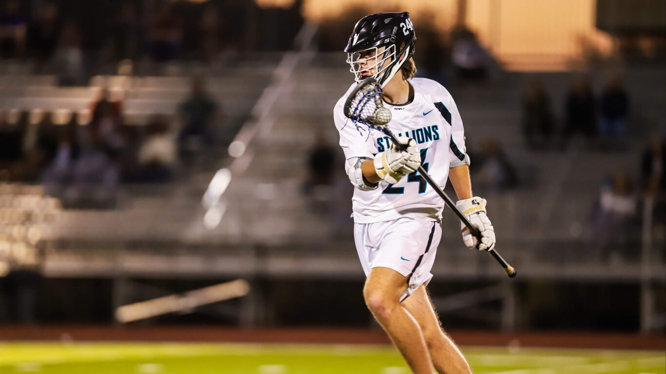 A boys' lacrosse player in action on a field.