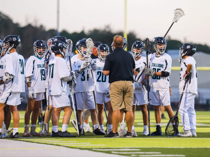 A group of lacrosse boys huddle on the field.