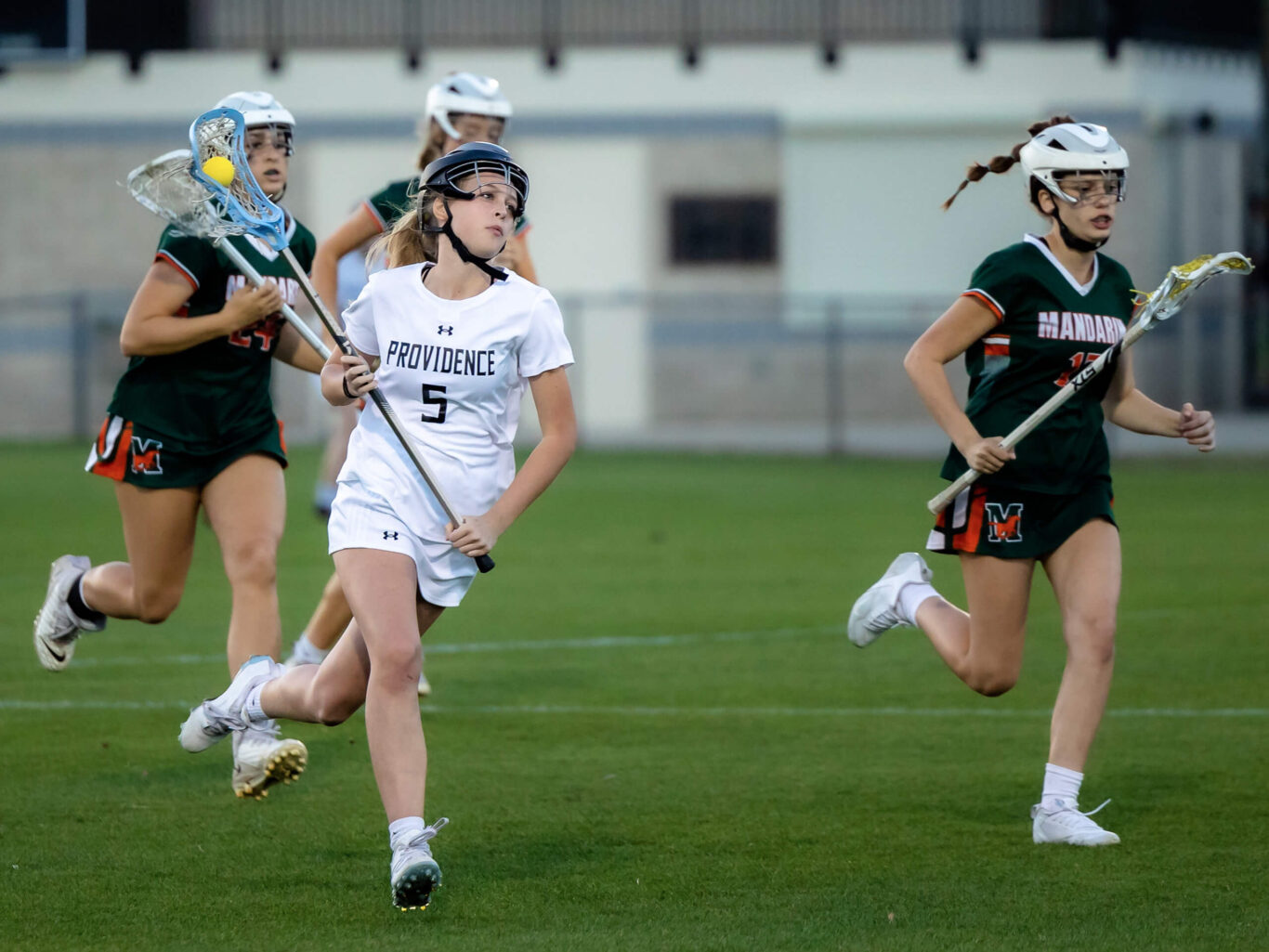 A group of girls playing lacrosse on a field.