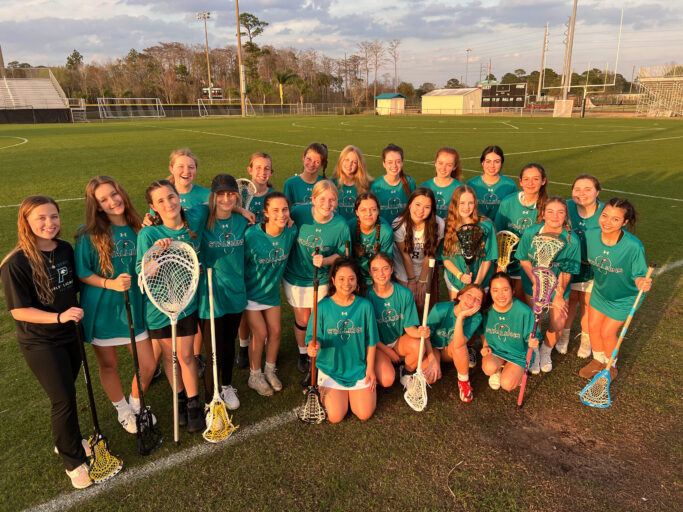 A group of girls posing for a picture with their lacrosse sticks.