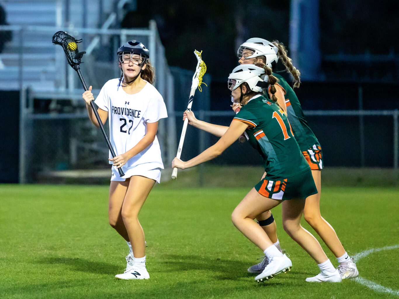 A group of girls playing lacrosse on a field.