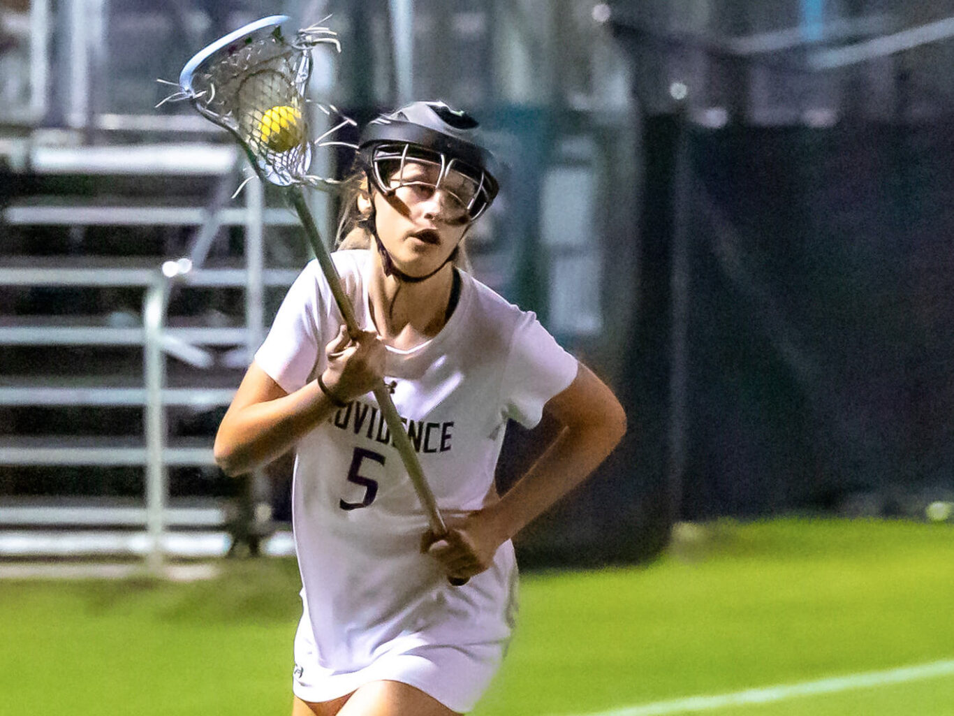 A female lacrosse player is running with a ball during a girls' lacrosse match.