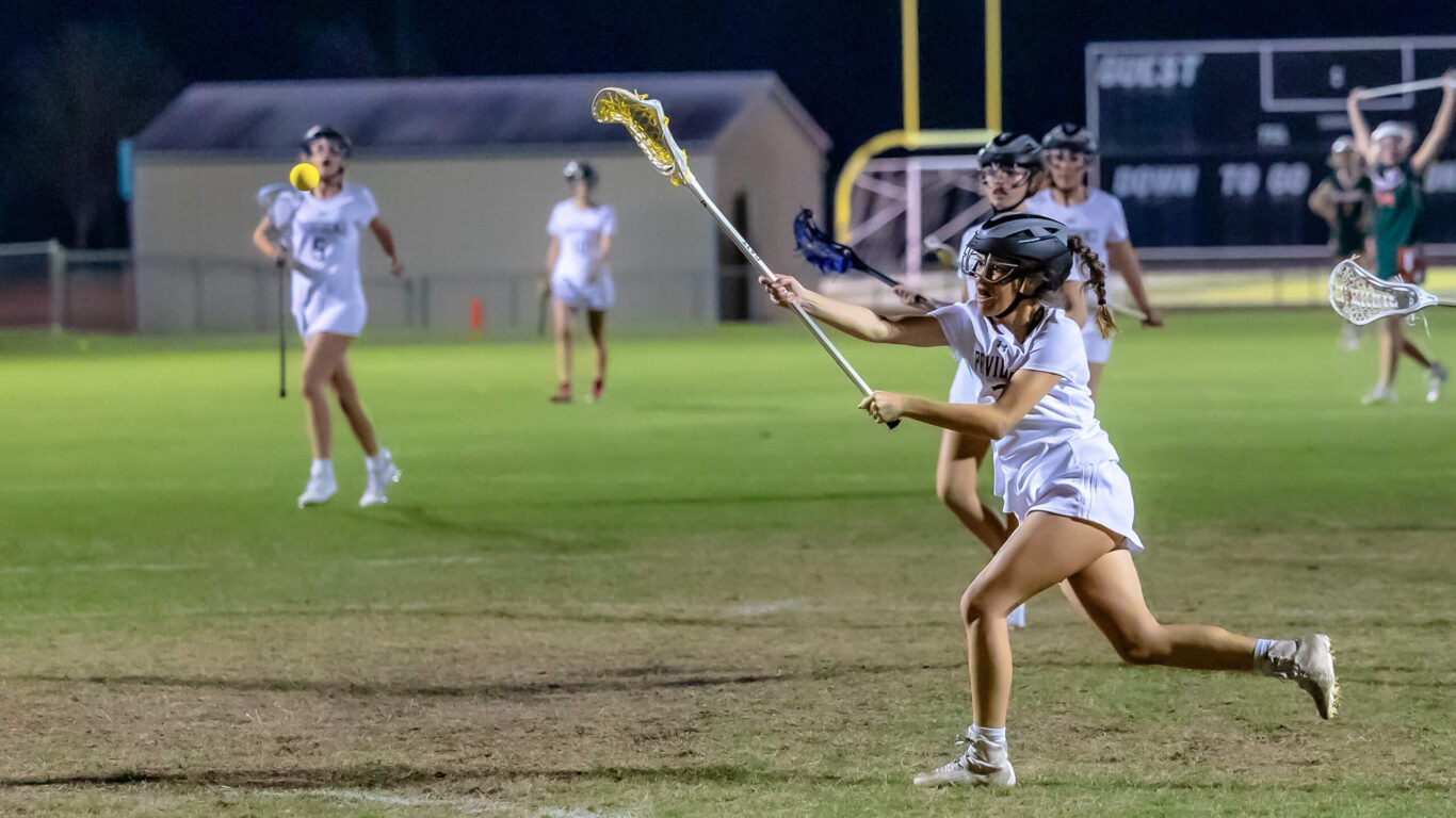 A female lacrosse player is sprinting on the field.
