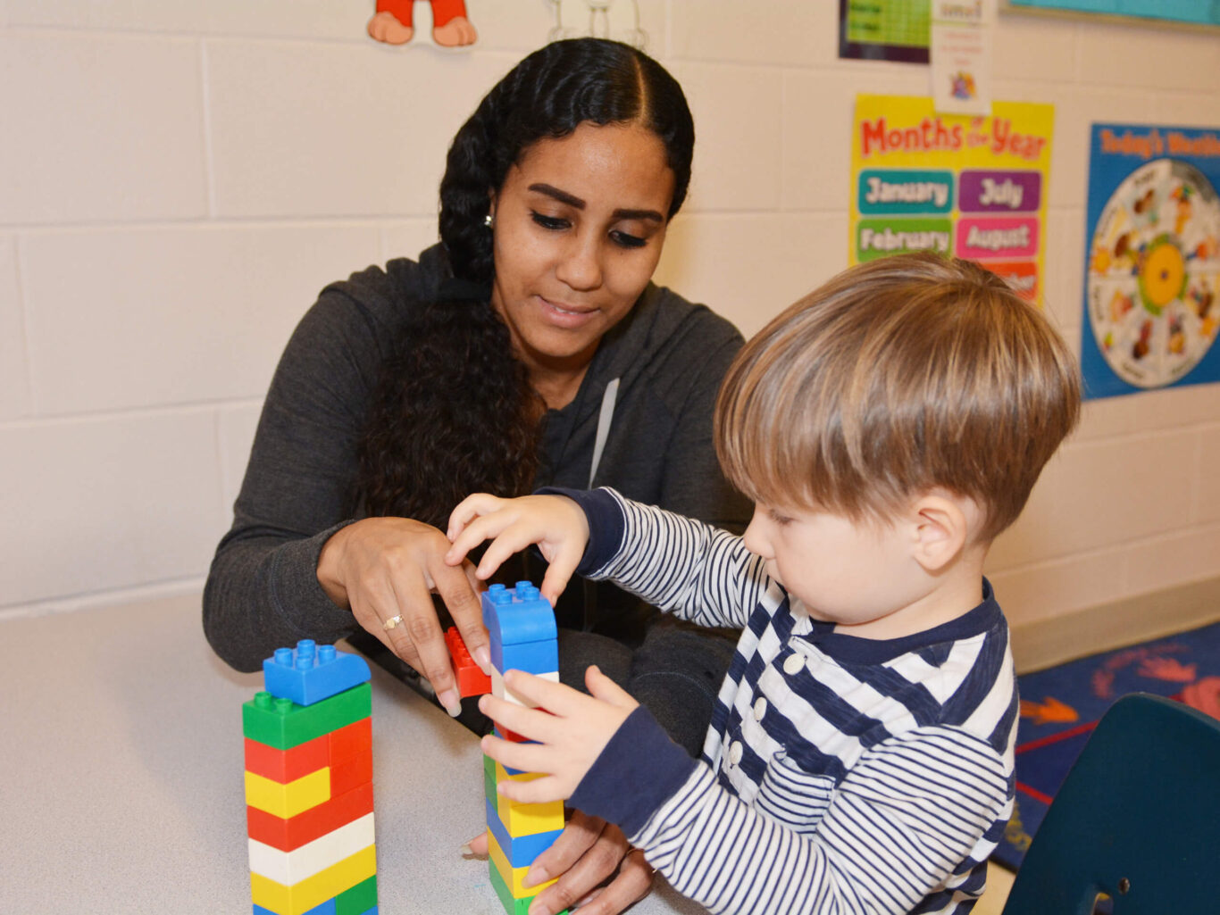 A preschooler and adult playing with legos in a classroom.