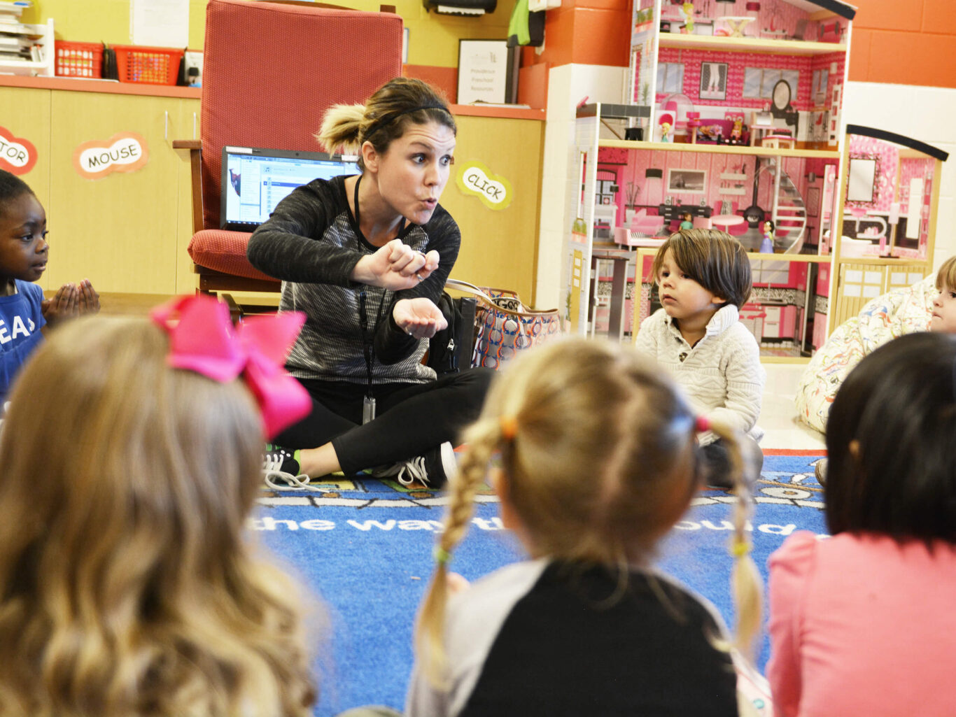 A preschool teacher is instructing a group of children in a classroom.