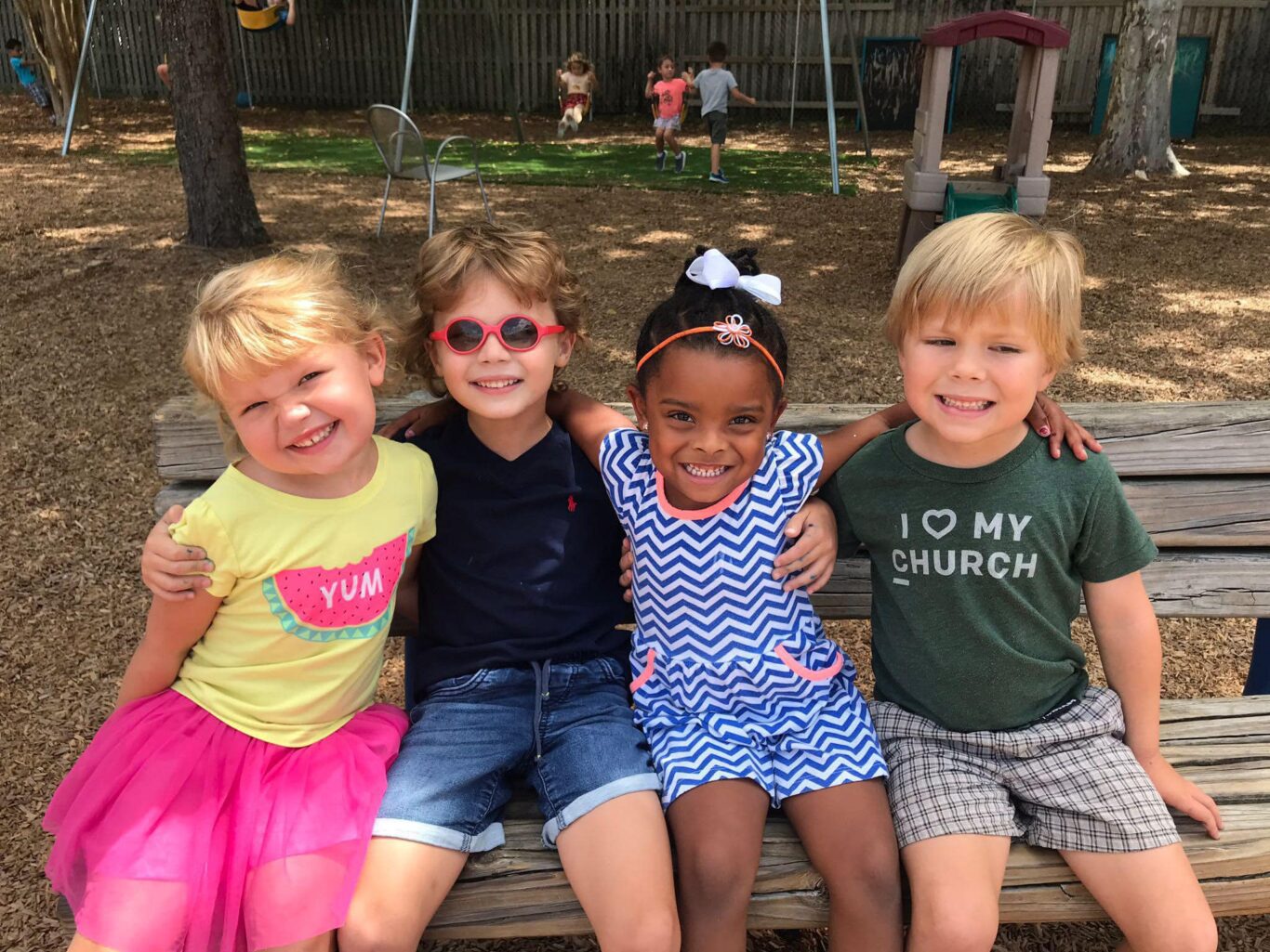Four preschool children posing for a picture on a park bench.