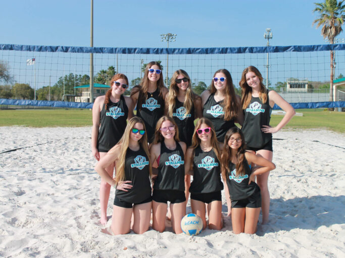A group of girls playing beach volleyball and posing for a photo.