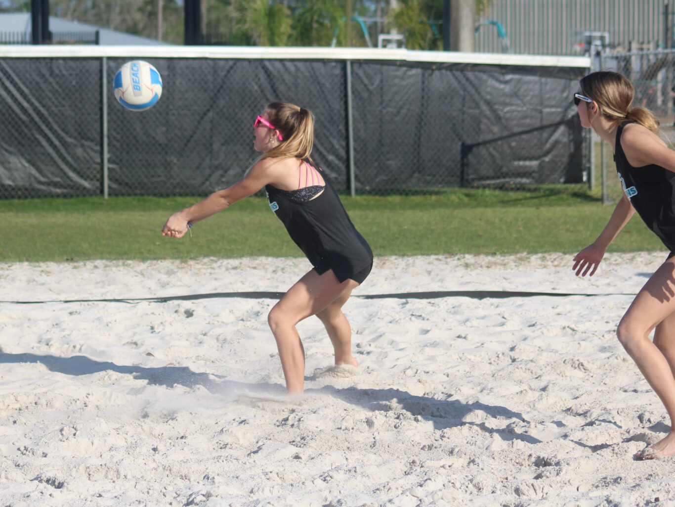 Two girls engaged in a game of beach volleyball on the sandy shore.