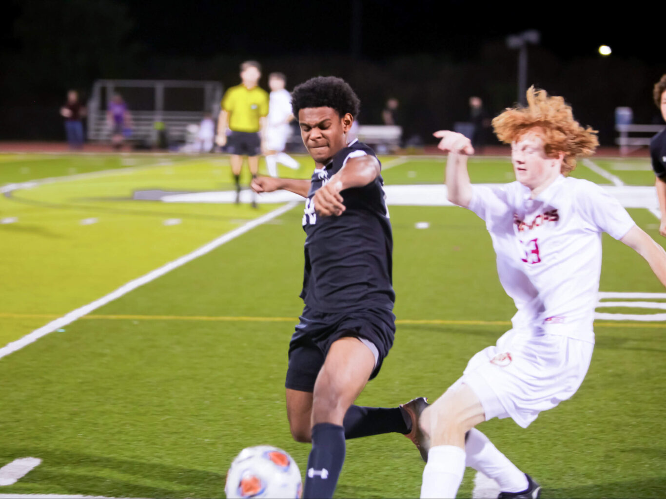 Two boys fighting for the soccer ball on a field.