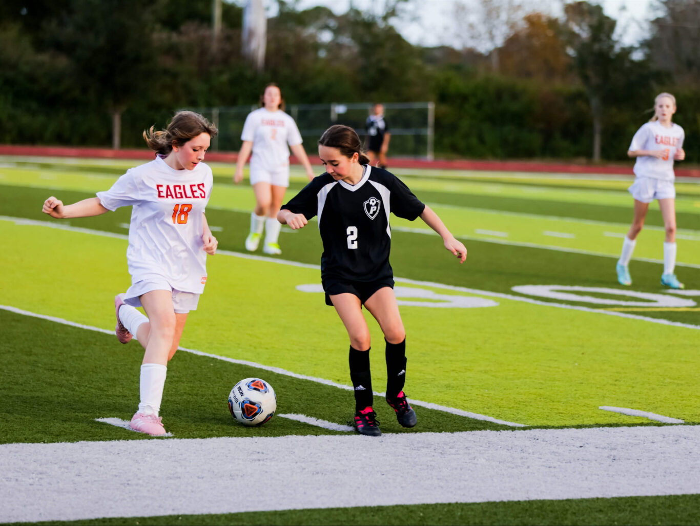 Two girls engaging in a game of soccer on a field.