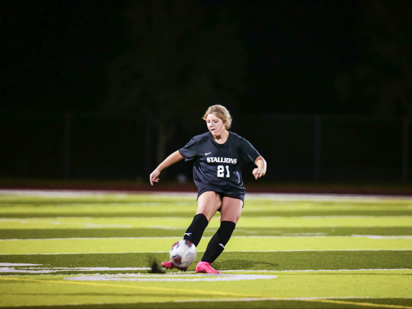 A soccer girl kicking a soccer ball at night.