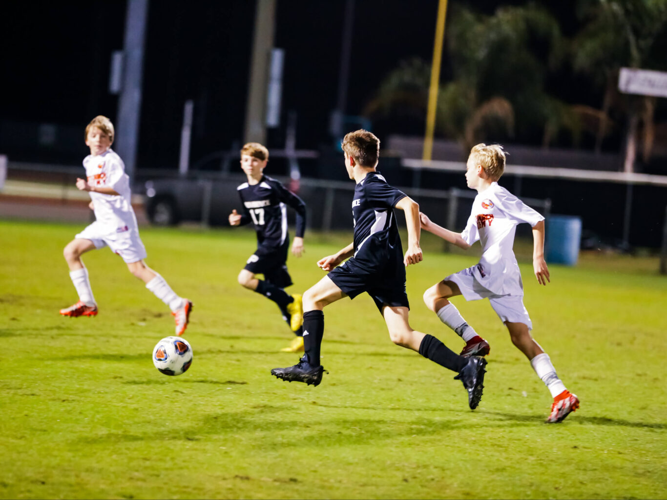 A group of boys passionately playing soccer on a field at night.