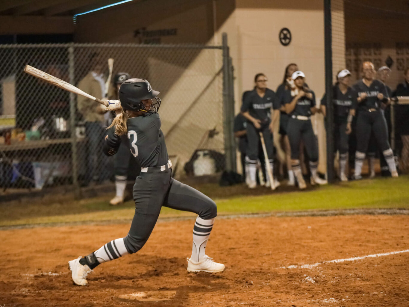 A softball player, a girl, swinging her bat at a ball.