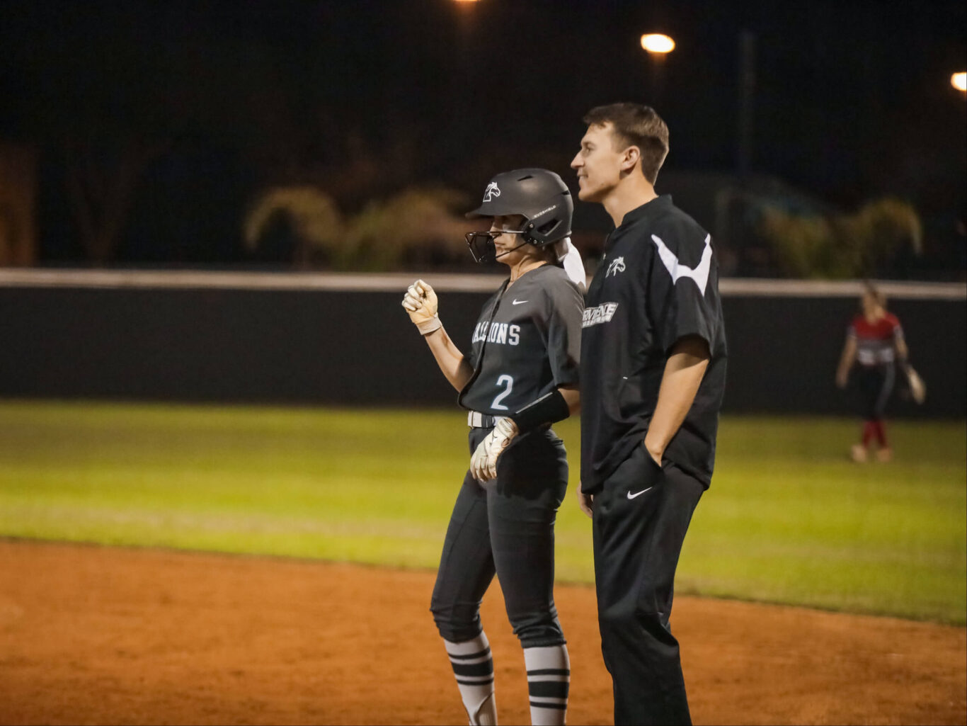 Two softball girls standing on the field at night.