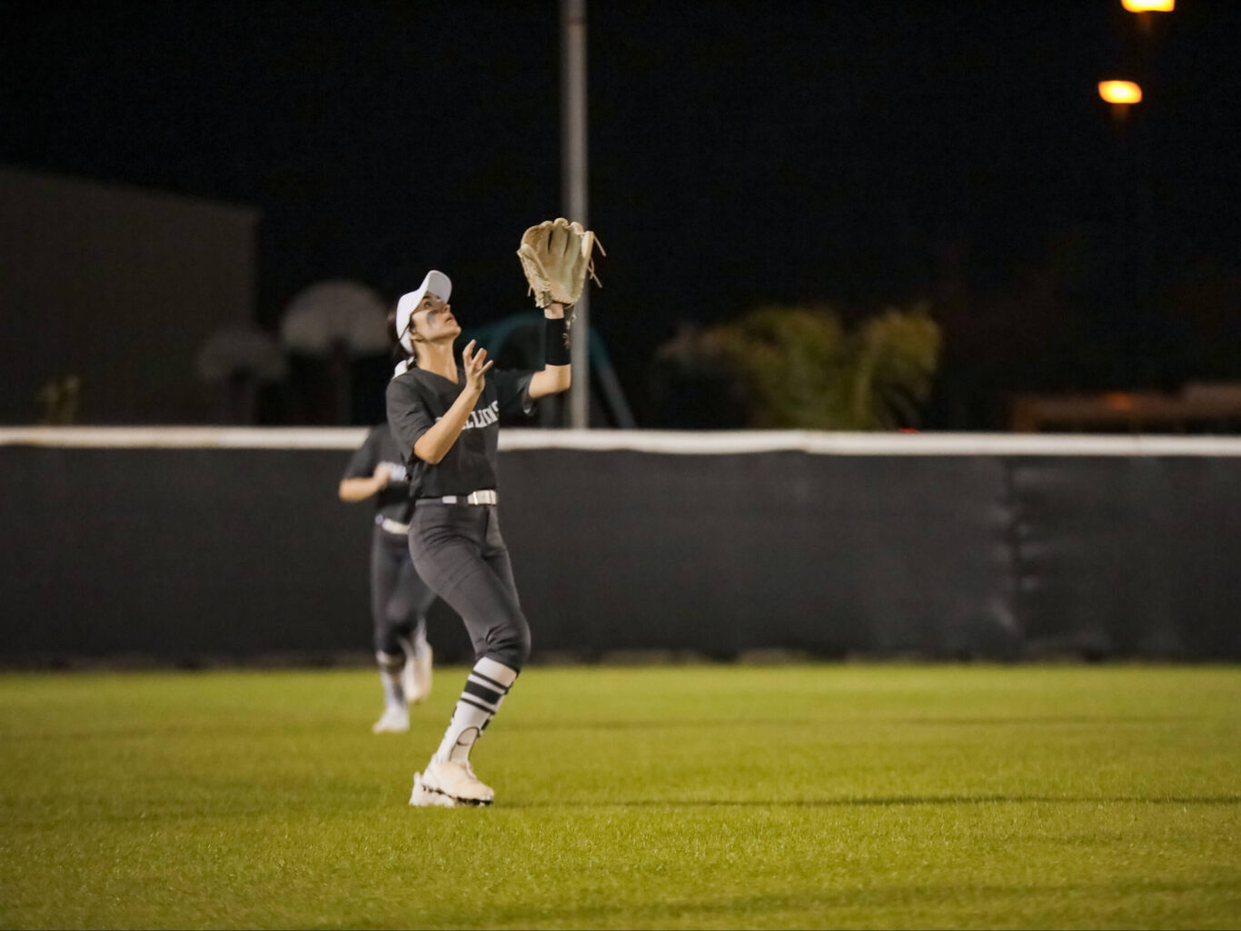 A girls softball player catching a ball on a field at night.
