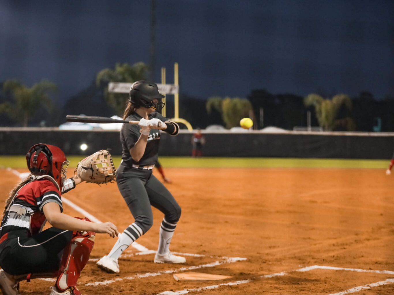 A girls softball player swinging a bat at a ball.