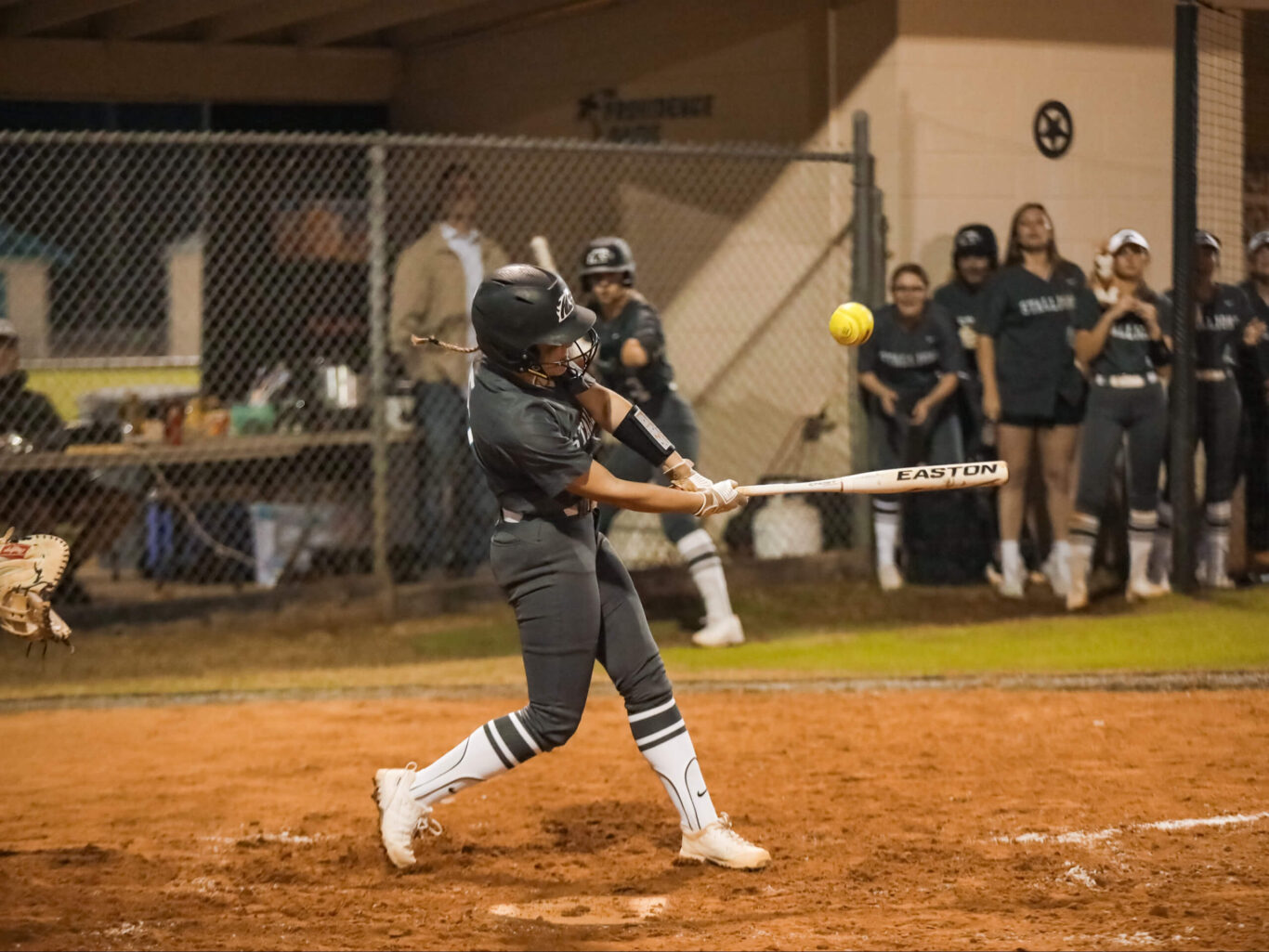 A softball player, a girl, swinging her bat at a ball.