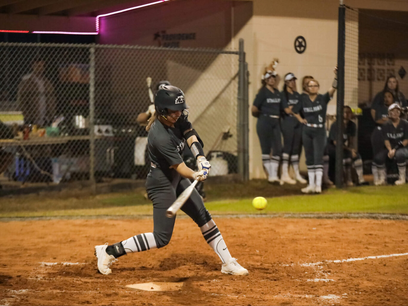 A softball player, typically a girl, swings at a ball during a game.