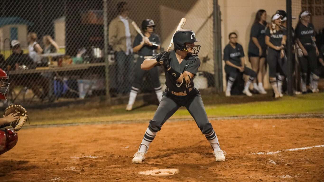 A girls' softball player swinging her bat at a ball.