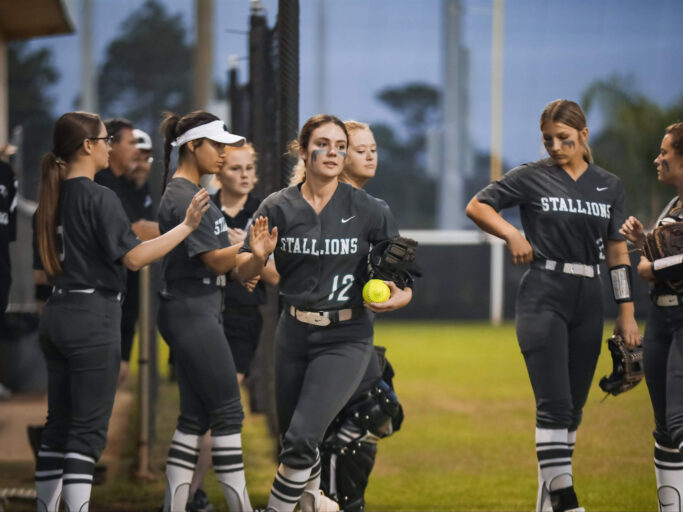 A group of softball players, most of them girls, standing on a field.