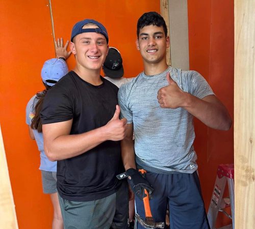 Two young men giving thumbs up in an orange room, showcasing their youthful energy and positive spirits.